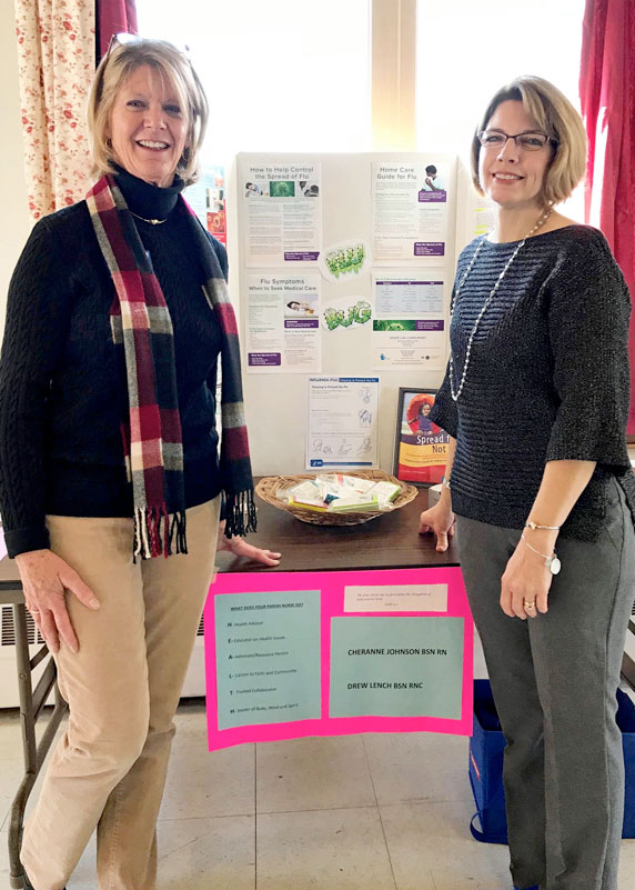 2 smiling nurses in front of display about staying healthy during flu season